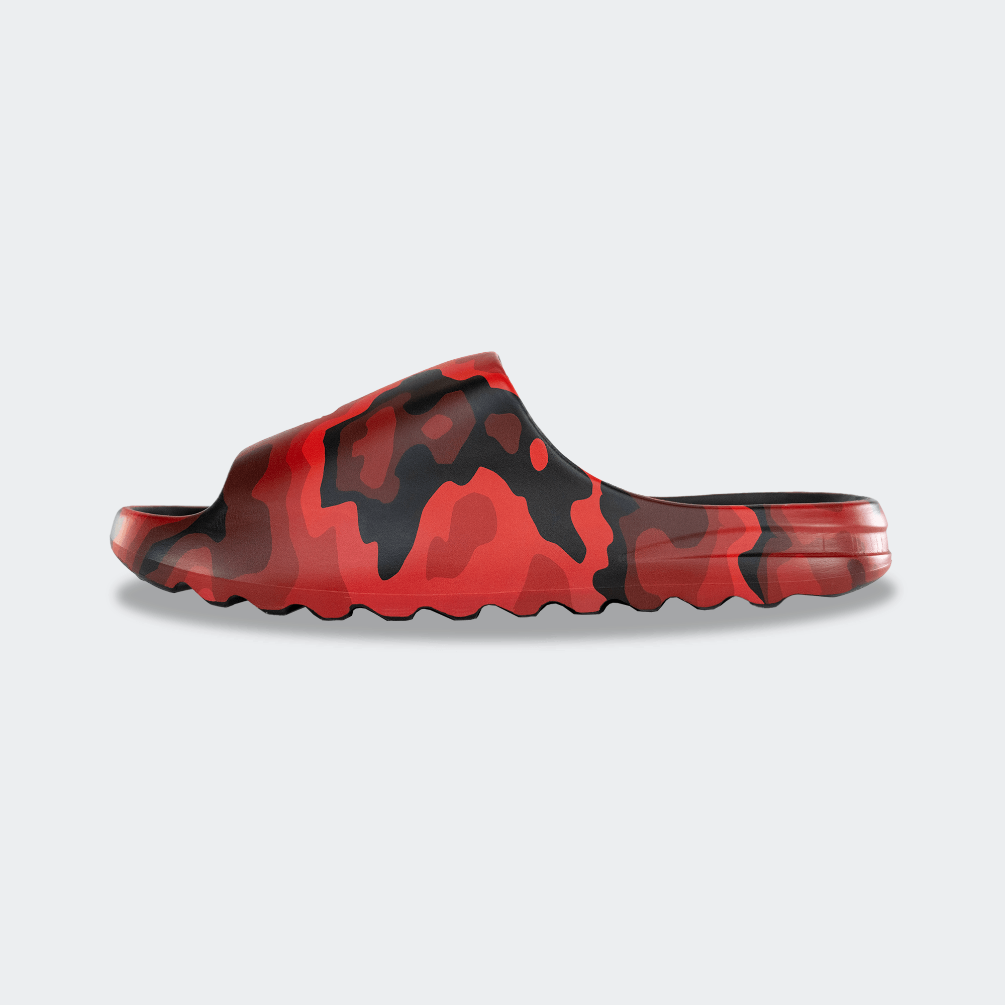 Side profile view of the inner side of a Combat Corner CRNR Foam Slide. The slide showcases the seamless, ergonomic design wrapped in a red and black Cinder Topo camouflage print, with a thick, contoured midsole and a serrated traction outsole visible along the bottom edge.