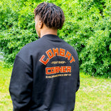 Rear view of a man with dreadlocks looking away, showcasing the large graphic on the back of a black Combat Corner crewneck sweatshirt. The orange and red block-letter design features an arched "Combat" above "Fight Shop" and "Corner," with "Milwaukee Since 2007" printed at the bottom.