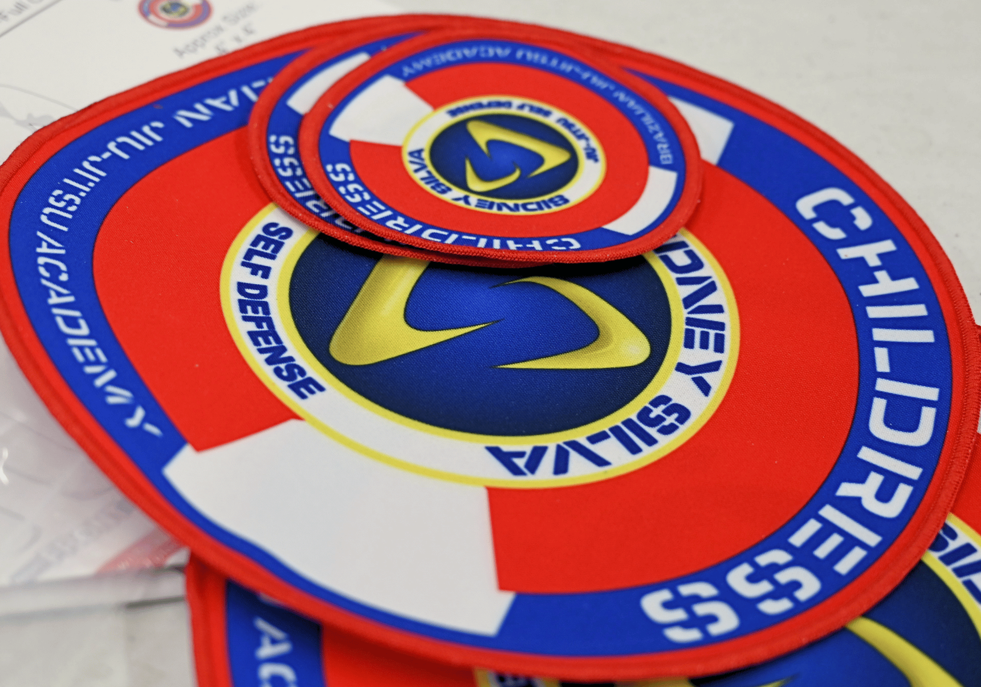 A close-up shot of circular red, blue, and yellow martial arts uniform patches for a Brazilian Jiu-Jitsu academy, showcasing custom gi patches and academy gear options from Combat Corner. 