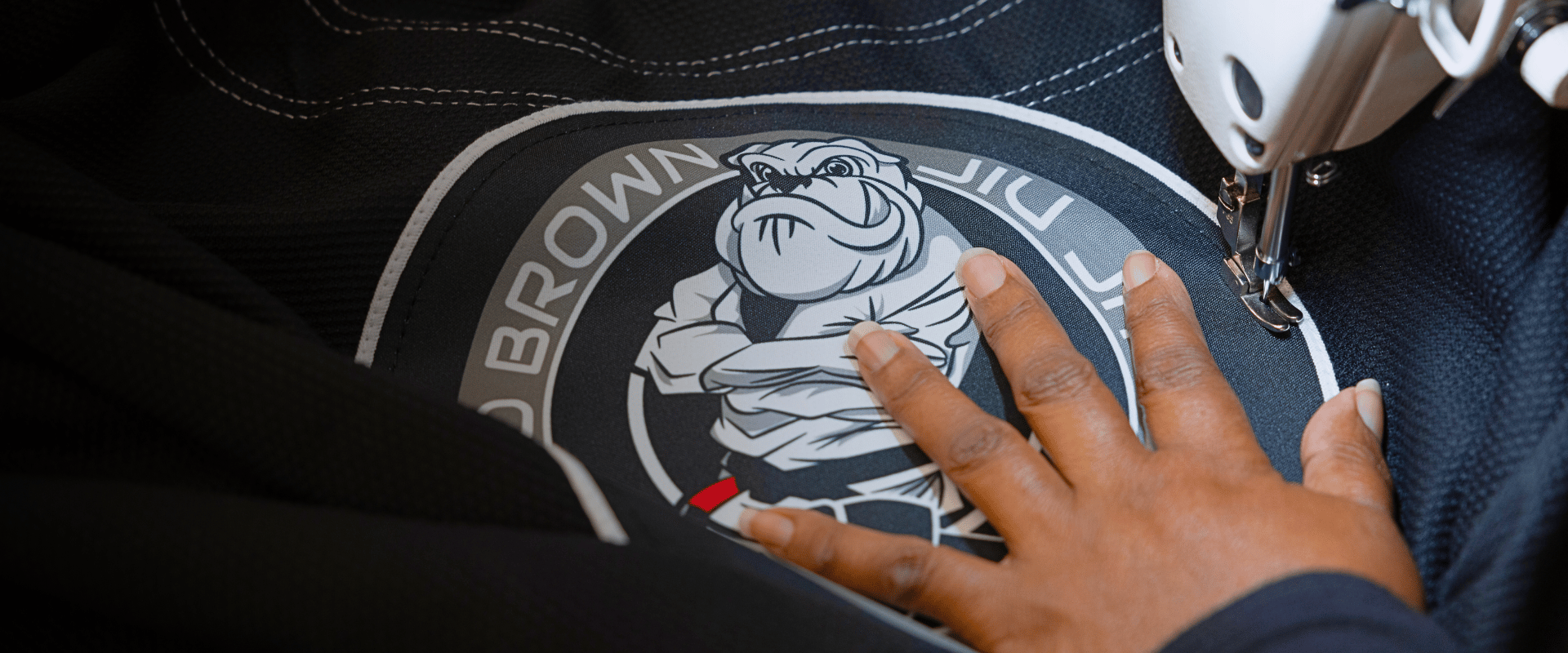 A close-up shot of a custom Todd Brown Jiu-Jitsu patch being sewn onto a black Combat Corner gi jacket using a professional sewing machine.