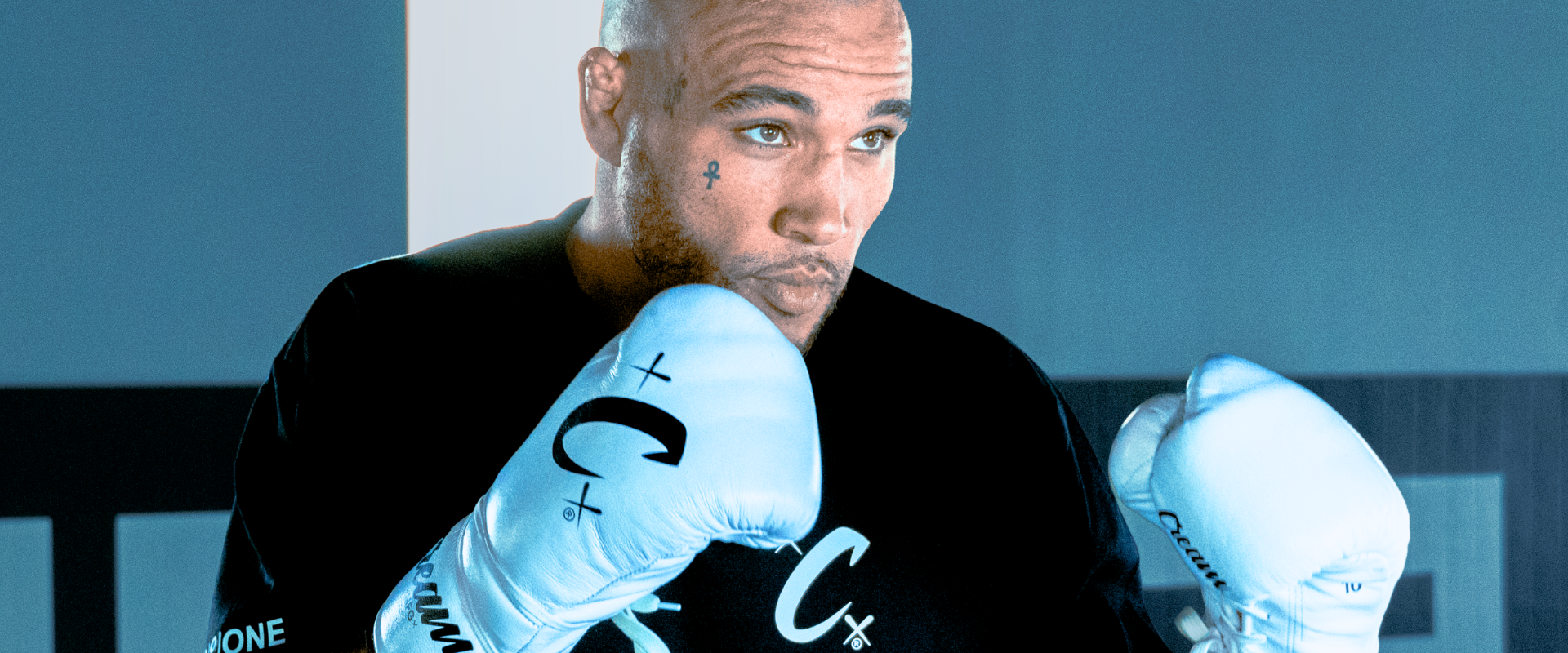 Medium shot of pro fighter Roland Dunlap in a boxing stance, wearing the black Cream Heavyweight T-Shirt and white Cream TM1 Boxing Gloves. 