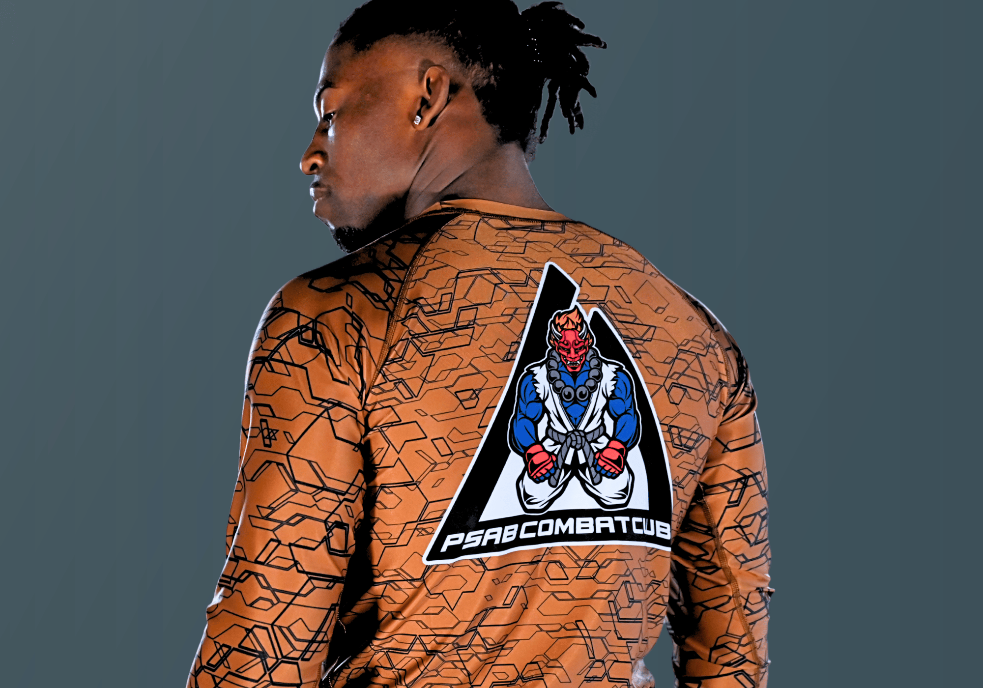 Rear view of an athlete modeling a custom tan Combat Corner rash guard featuring an intricate geometric line pattern and a large Oni demon martial arts graphic on the back.