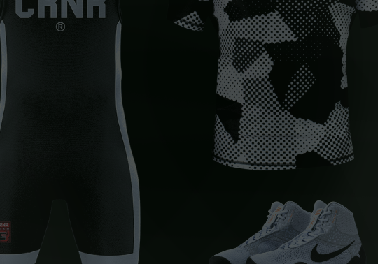 A product display of black combat sports gear from Combat Corner against a dark background, including singlets, rash guards, and wrestling shoes.