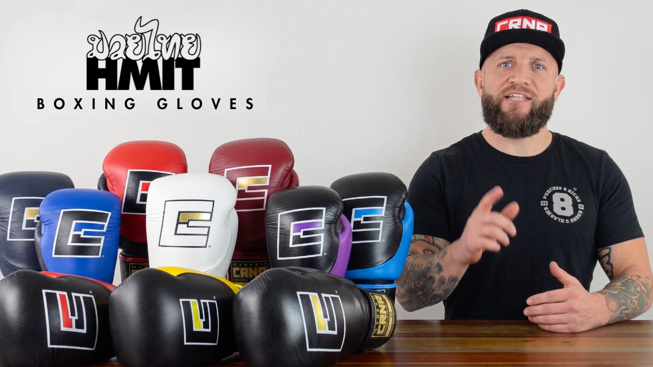 A YouTube thumbnail image featuring pro fighter Dan LaSavage in a black CRNR cap giving a product walkthrough of HMIT Boxing Gloves and gesturing toward an array of colorful Combat Corner HMIT Boxing Gloves lined up on a wooden table. 