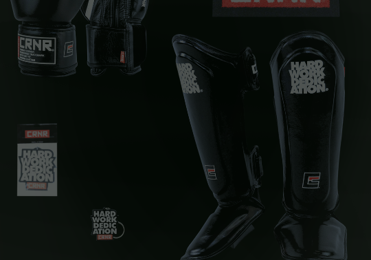 A product display of black combat sports gear from Combat Corner against a dark background, including shin guards, key chains, and boxing gloves.