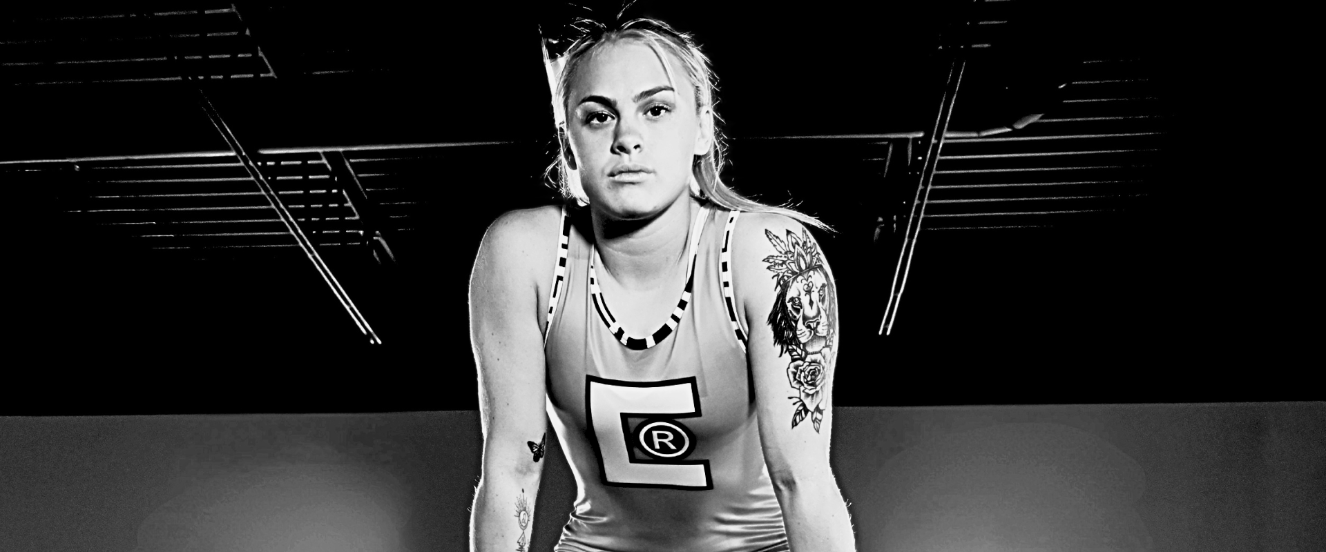 High-contrast black and white portrait of female wrestler champion Mateah Roehl looking forward, wearing a Combat Corner wrestling singlet with a large chest logo. 