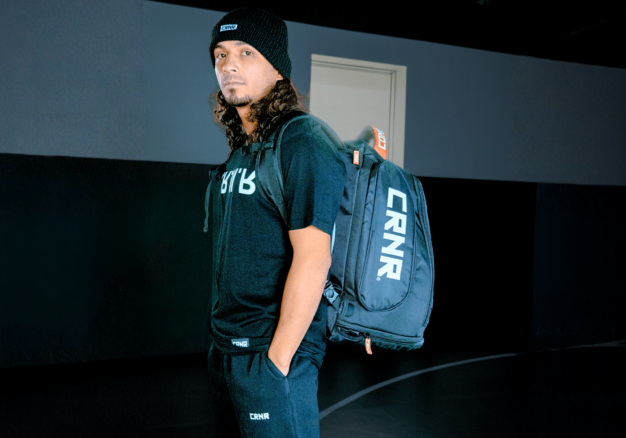 Three-quarter profile shot of Oktagon Flyweight Champion Elías García finishing a training session and wearing Combat Corner’s black Trademark beanie, Up DN IN OUT T-Shirt, and CRNR Relaxed Sweatpants, Expand Pack Gear Bag. 