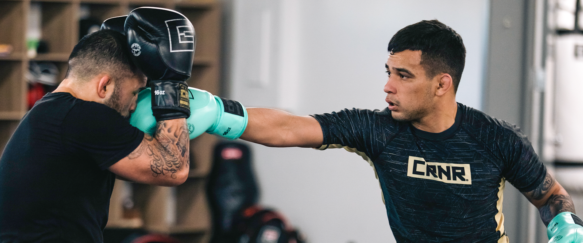 An action shot of professional fighter Christian Rodriguez throwing a straight left punch during a sparring session, wearing Combat Corner’s Fiber Rash Guard and mint HMIT Boxing Gloves. 