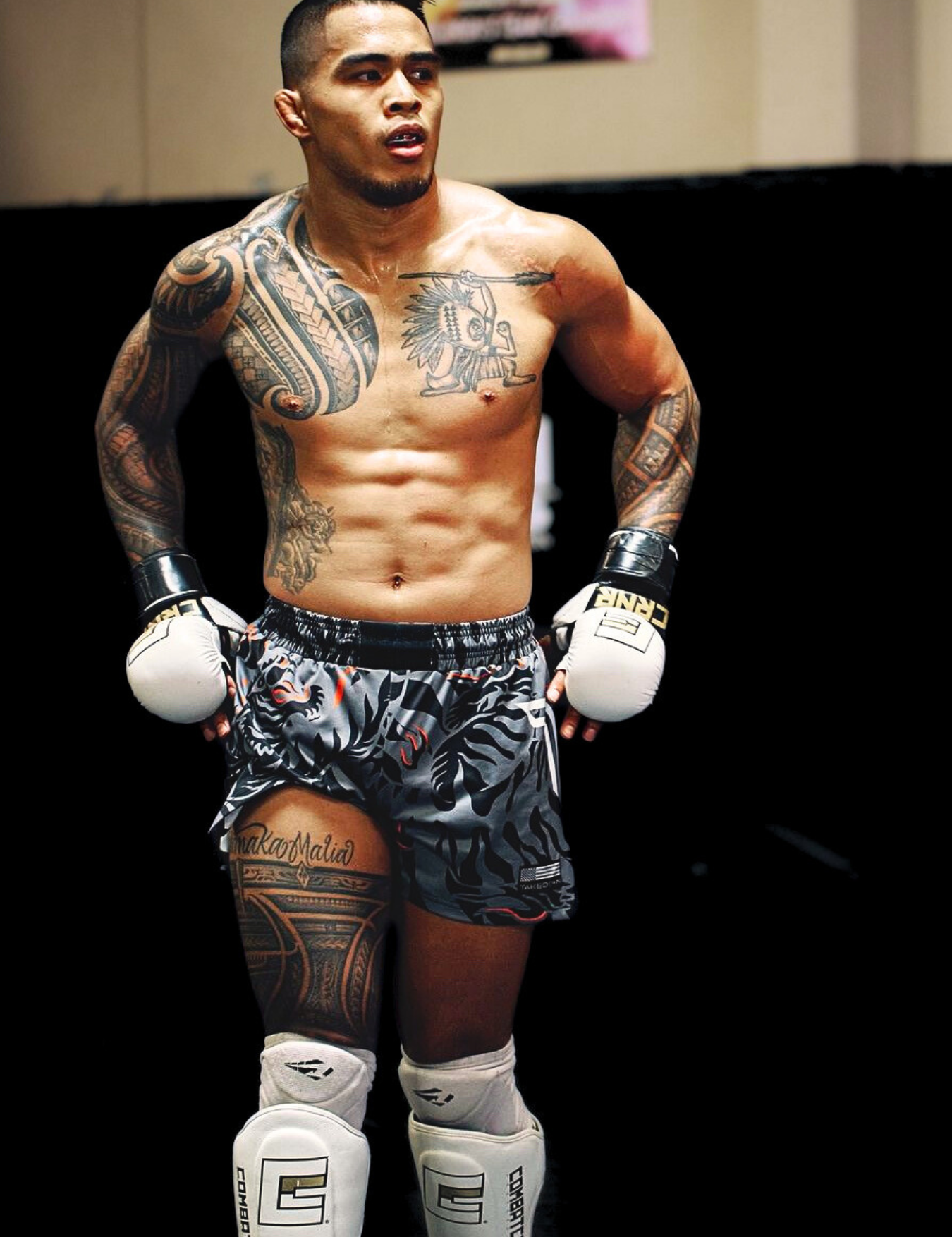 Full-body shot of a heavily tattooed UFC Fighter and Combat Corner Pro Team Member Kai Kamaka walking forward, wearing Combat Corner’s Muay Thai Shorts, MMA Spar Gloves, and HMIT Shin Guards.