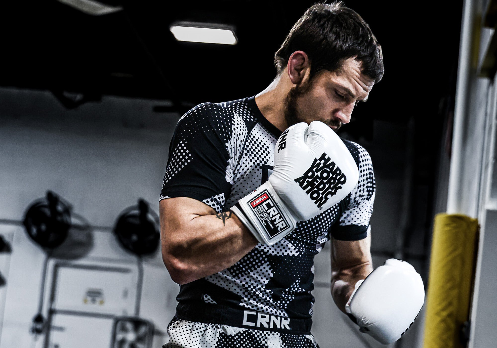 Medium close-up portrait of professional fighter Nick Klein looking down thoughtfully while wearing Combat Corner’s white HWD Boxing Gloves and black and white patterned Camcow Rash Guards and Combat Trainer Fight Shorts. 
