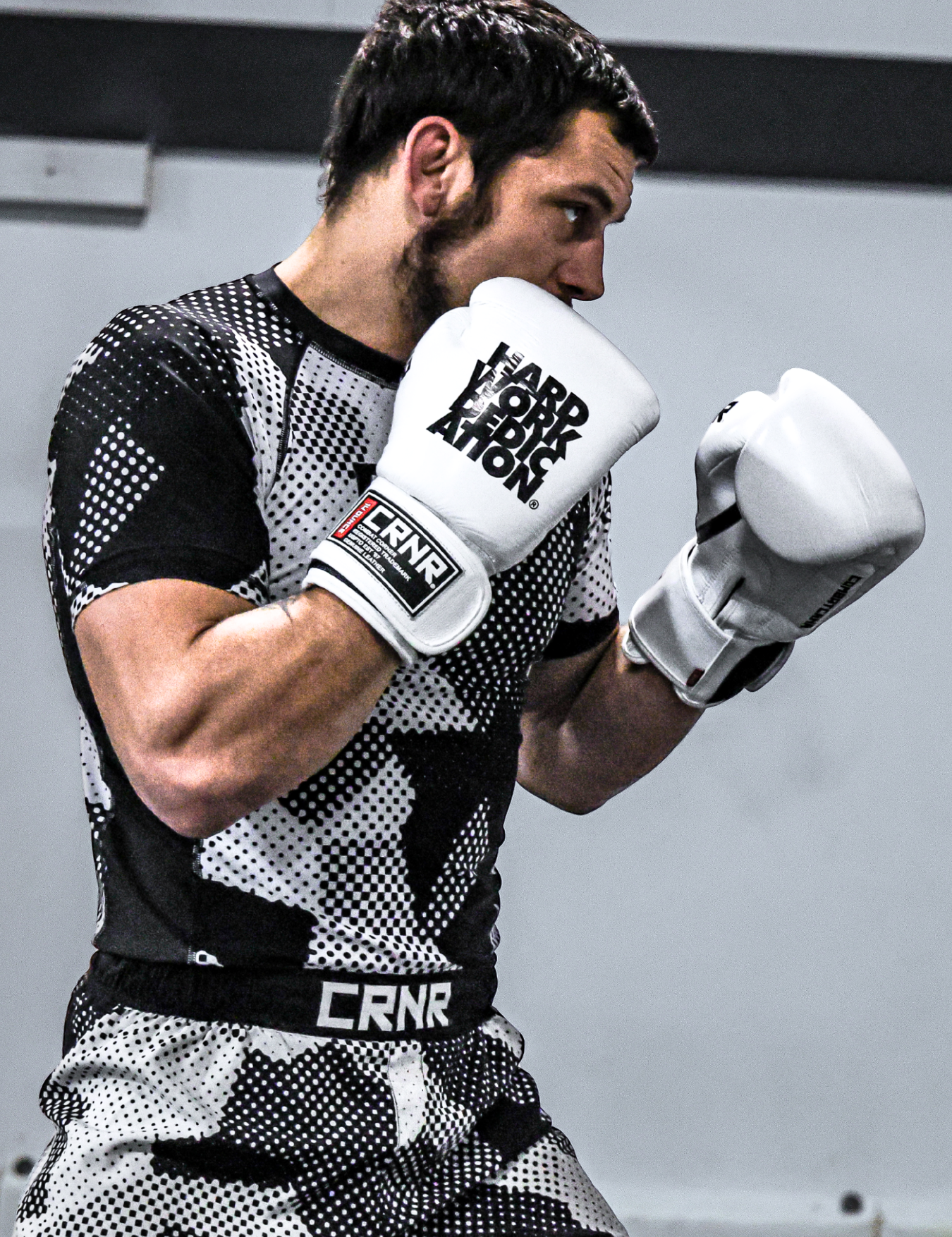 Profile shot of pro fighter and Combat Corner Pro Team Member Nick Klein in a boxing stance wearing Combat Corner’s Camcow Rash Guard and Camcow Cross Trainer Fight Shorts, showcasing Combat Corner’s white HWD Boxing Gloves that feature bold text reading "Hard Work Dedication" and a "CRNR" wrist label. 