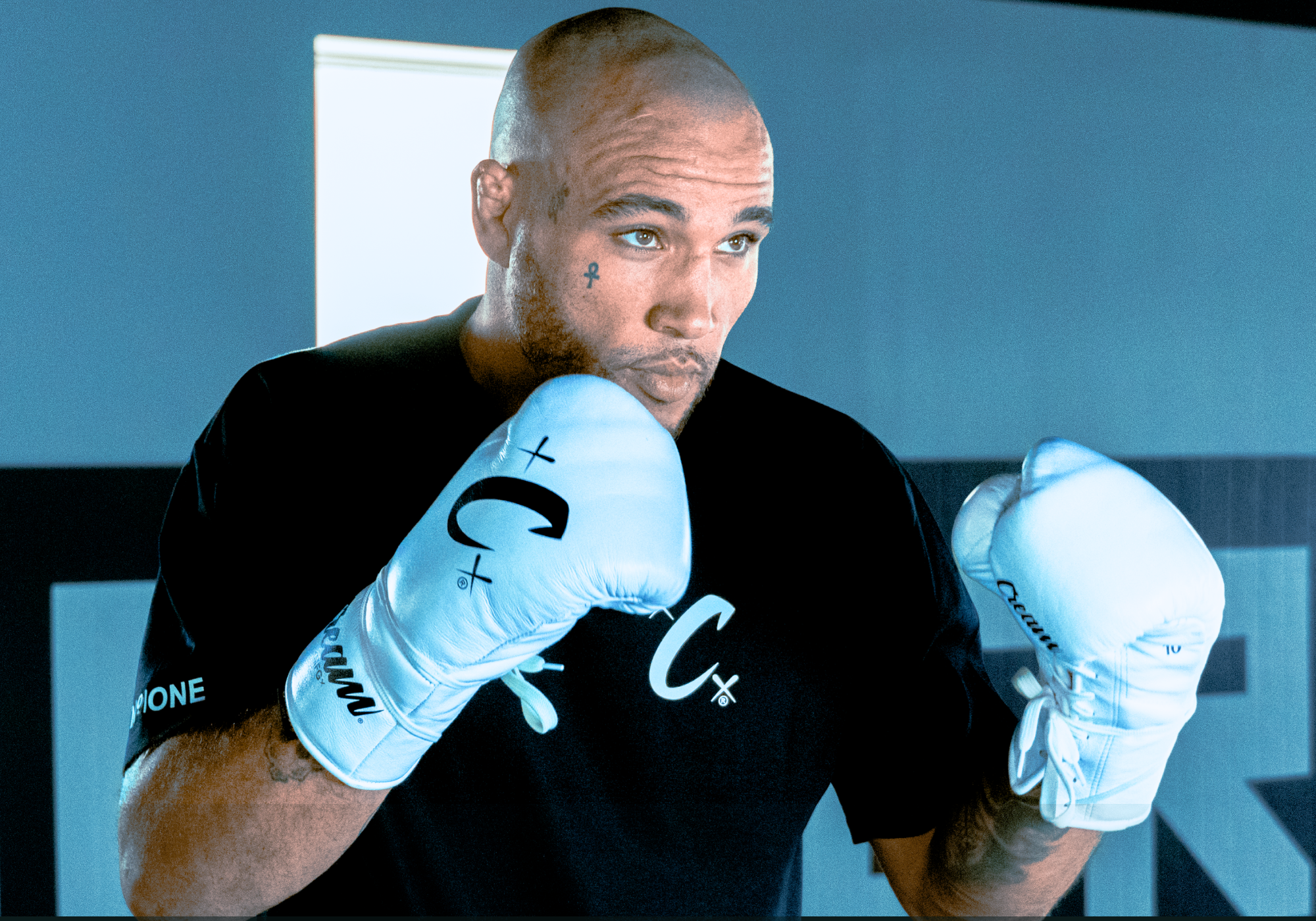 Medium shot of a pro fighter Roland Dunlap in a boxing stance, wearing Combat Corner’s black Cream Ultra Heavyweight T-Shirt and training with white Cream TJ1 Boxing Gloves. 