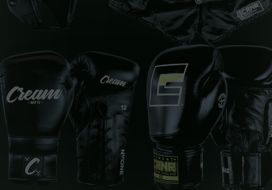 A product display of black combat sports gear from Combat Corner against a dark background, including a sparring headgear, satin Muay Thai shorts, and two different pairs of black leather boxing gloves. 