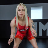 Photo of a college female athlete wearing Combat Corner’s premium Red USA Wrestling Singlet. The woman faces the camera and crouches in a wrestling pose in Combat Corner’s collegiate wrestling training gym. This USA Red Singlet is part of Combat Corner’s Competition Singlet Series and is fully UWW Compliant to give you champion performance in Freestyle and Greco-Roman wrestling.