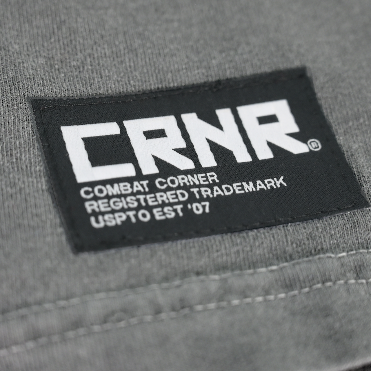 Product photo of Combat Corner’s exclusive Pinnin’ & Winnin’ Relaxed Tee. This photo shows a detail, close up on the delux embroidered CRNR logo tag on the side of Combat Corner’s Pinnin’ & Winnin’ Faded Navy Relaxed Tee. This CRNR tee offers the same softness and comfort as your favorite, well-loved vintage tee.