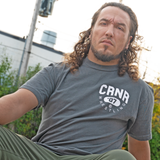 Product photo of Combat Corner’s exclusive Pinnin’ & Winnin’ Relaxed Tee. This photo shows a young man wearing Combat Corner’s Pinnin’ & Winnin’ Faded Navy Relaxed Tee. The photo shows the front of the CRNR tee. The man is outside his local gym after his workout and wrestling training session. This CRNR tee offers the same softness and comfort as your favorite, well-loved vintage tee.
