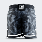 Rear view of Combat Corner CRNR ISO black fight shorts. Displays a centered, square black interlocking "CRNR" logo patch on the gathered elastic waistband. A thin white horizontal stripe runs just above the black bottom hem on both legs, and a small white logo print sits on the lower right leg.