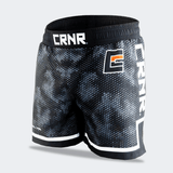 Three-quarter front-left view of Combat Corner CRNR ISO black fight shorts. Highlights the prominent square orange-accented logo on the front hip alongside the massive vertical white "CRNR" branding on the side panel. The white trim contrasts cleanly against the black lower border and side slit.