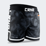 Three-quarter front-right view of Combat Corner CRNR ISO black fight shorts. Focuses on the right leg, displaying the subtle "ISOSUTURE // HYBRID" white text print near the bottom hem line. The full coverage of the dark grey honeycomb-like camo pattern across the front panel is clearly visible.