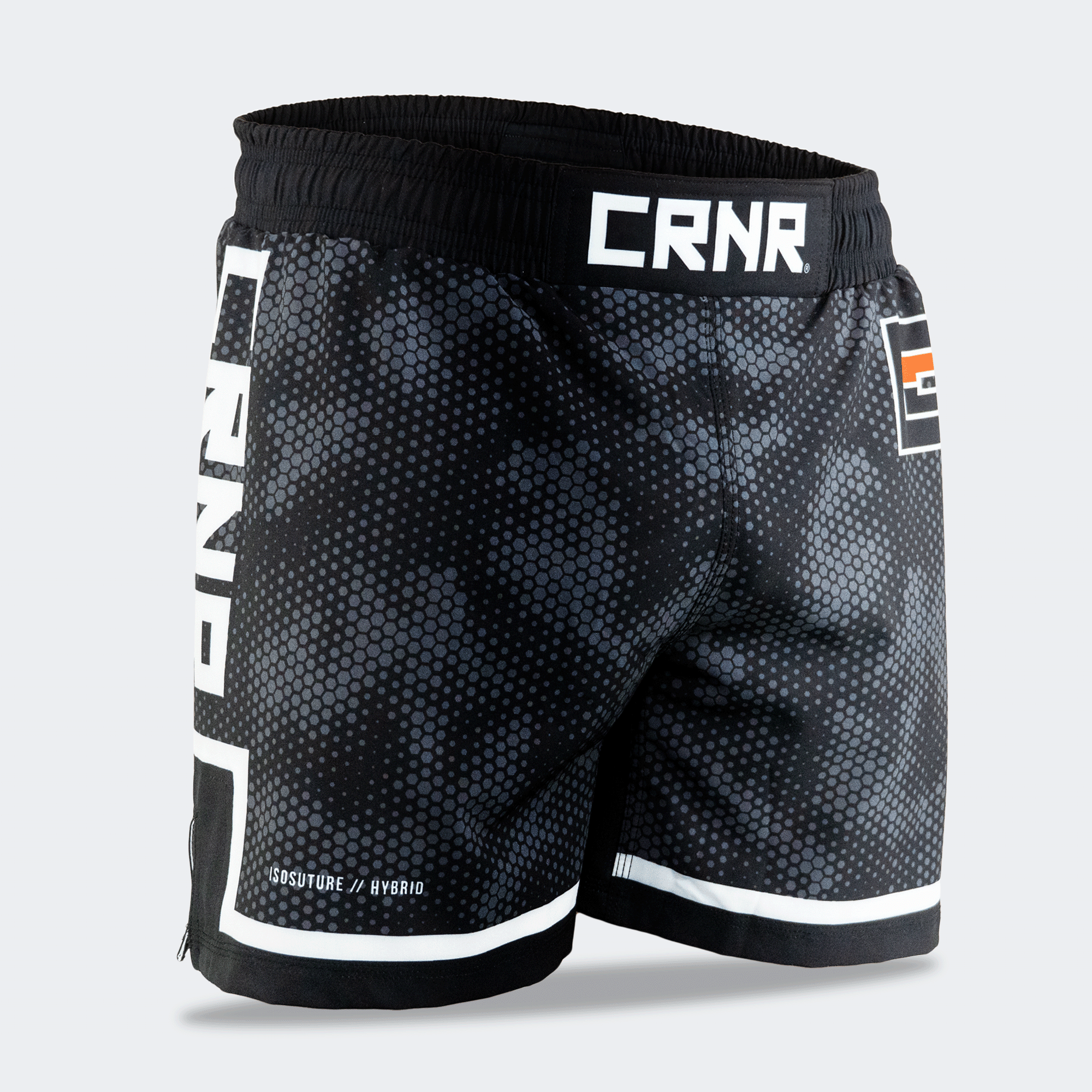 Three-quarter front-right view of Combat Corner CRNR ISO black fight shorts. Focuses on the right leg, displaying the subtle "ISOSUTURE // HYBRID" white text print near the bottom hem line. The full coverage of the dark grey honeycomb-like camo pattern across the front panel is clearly visible.
