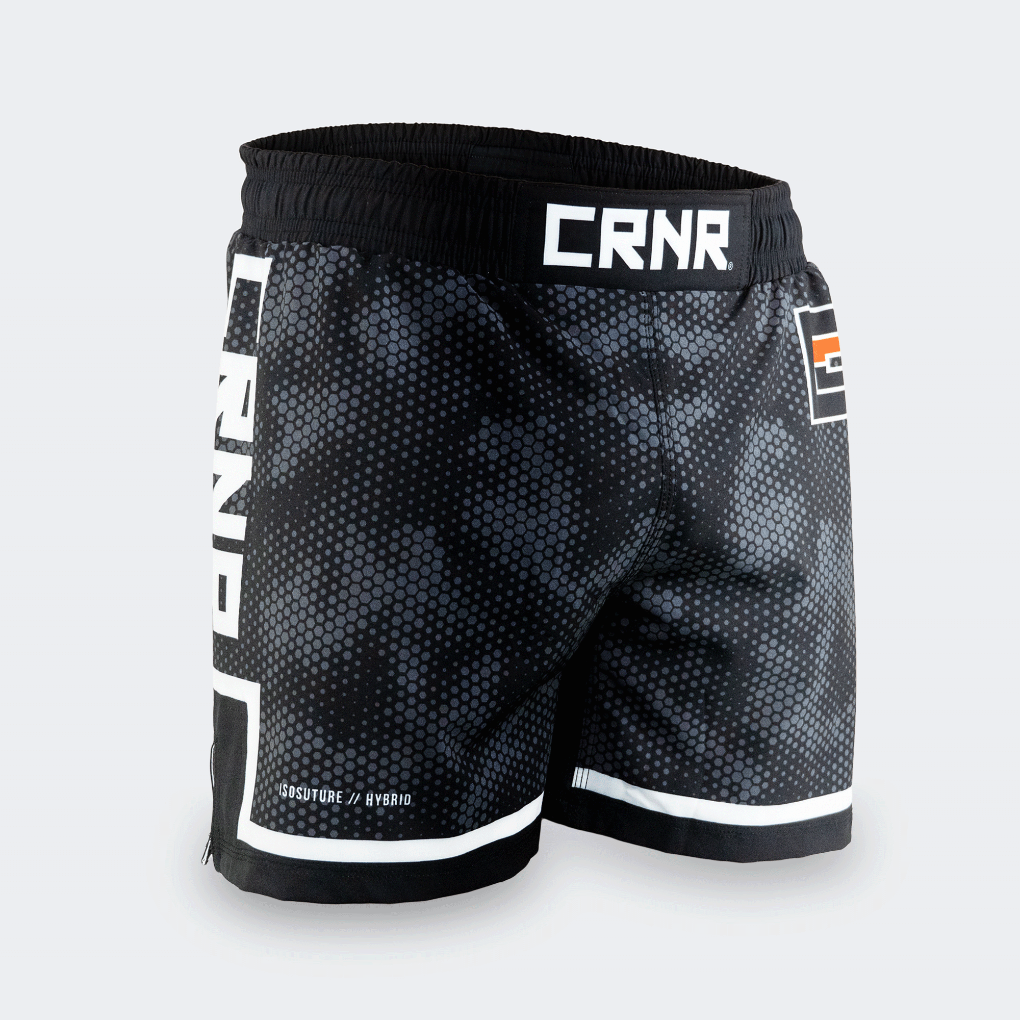 Three-quarter front-right view of Combat Corner CRNR ISO black fight shorts. Focuses on the right leg, displaying the subtle "ISOSUTURE // HYBRID" white text print near the bottom hem line. The full coverage of the dark grey honeycomb-like camo pattern across the front panel is clearly visible.