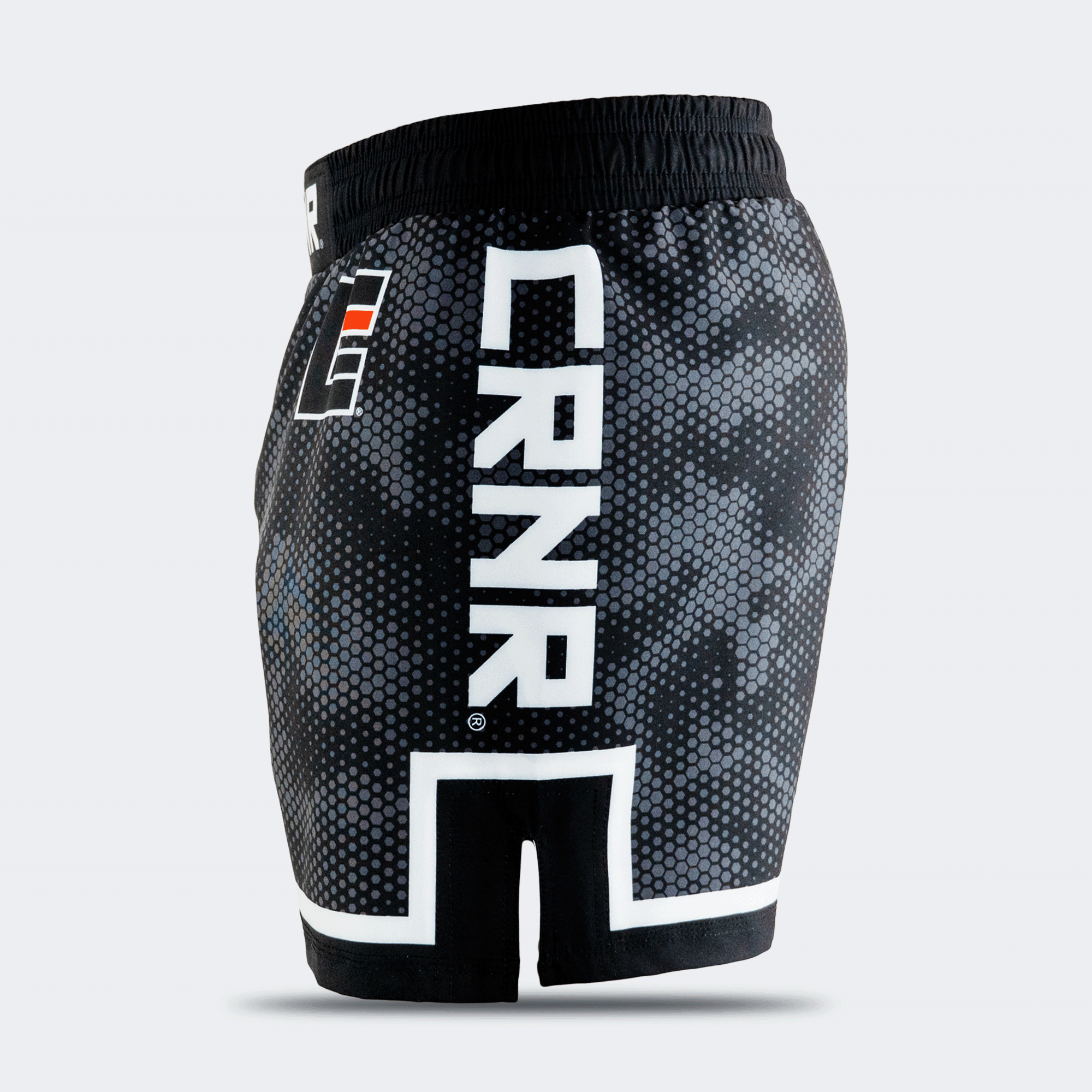 Left side profile of Combat Corner CRNR ISO black fight shorts. Features a large, vertical white "CRNR" logo running down the thigh, framed above a distinct white geometric border. A black side slit cut-out splits the lower hemline, and a small square orange and white logo is visible near the front hip.