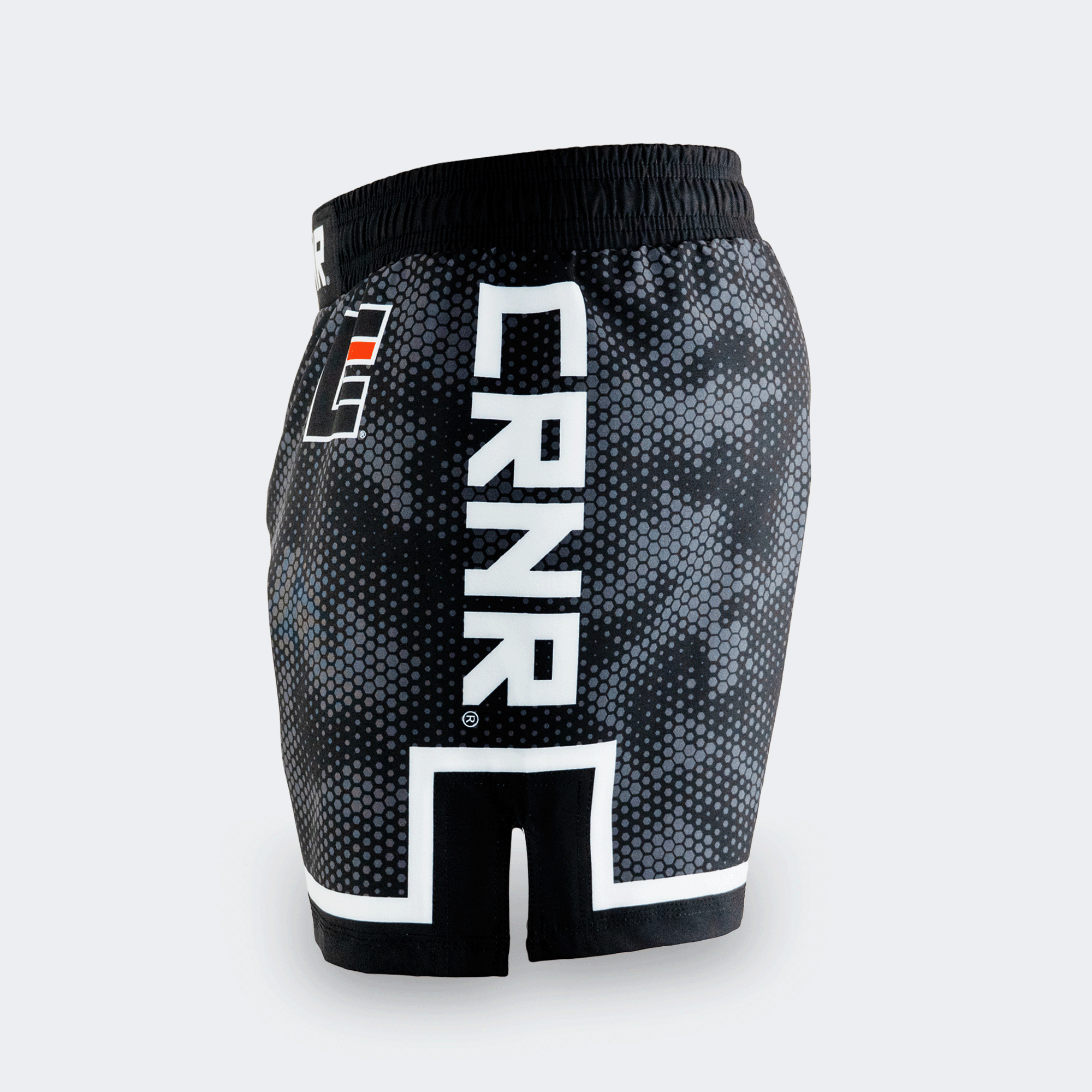 Left side profile of Combat Corner CRNR ISO black fight shorts. Features a large, vertical white "CRNR" logo running down the thigh, framed above a distinct white geometric border. A black side slit cut-out splits the lower hemline, and a small square orange and white logo is visible near the front hip.