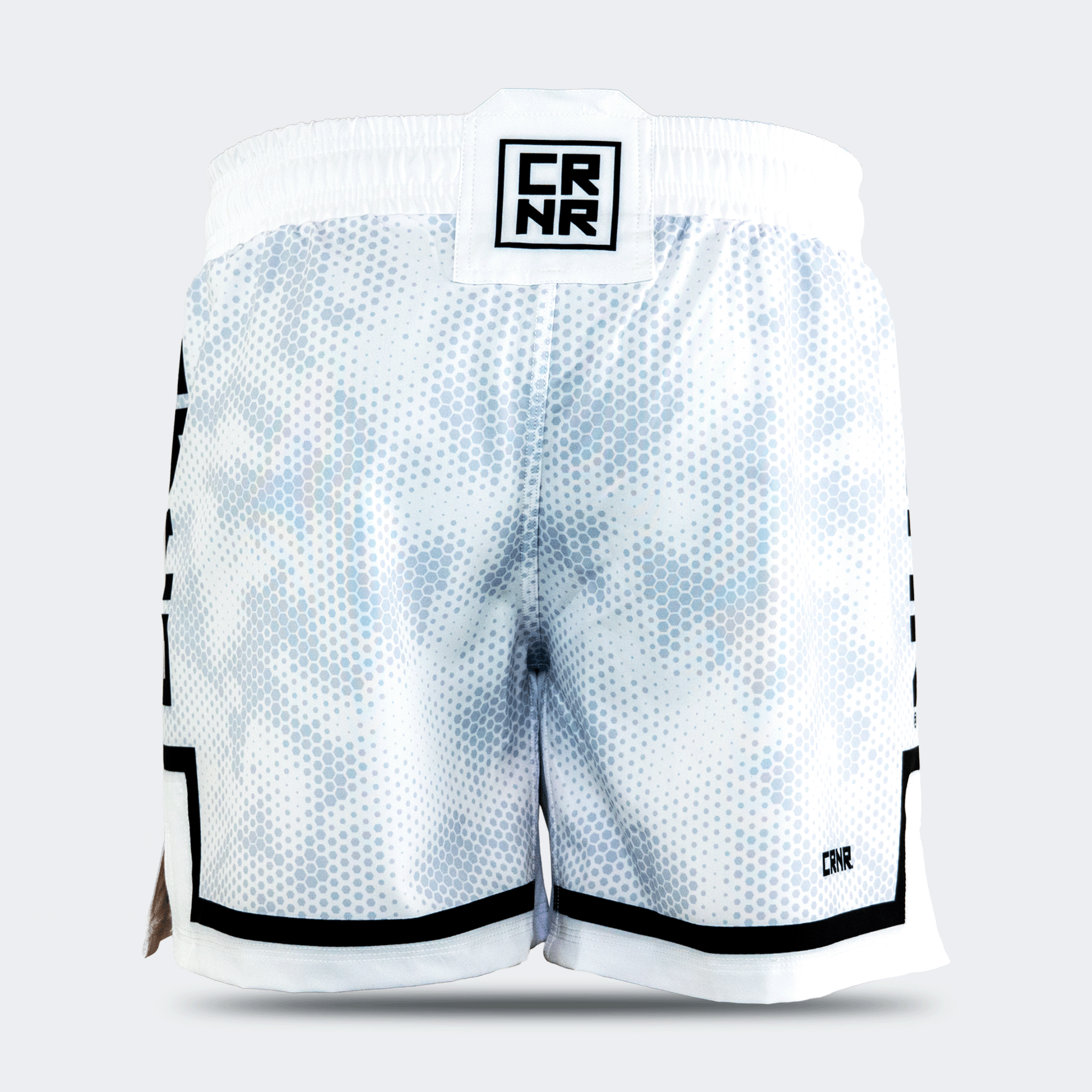 Rear view of the white Combat Corner hybrid fight shorts against a light grey background. The back displays the continuous hexagonal digital camo pattern, a square black and white "CRNR" logo patch on the center of the waistband, and a small black "CRNR" logo printed near the lower right hem.