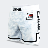 Three-quarter front-left view of the white Combat Corner hybrid fight shorts against a light grey background. This angle highlights the vertical black "CRNR" branding running down th