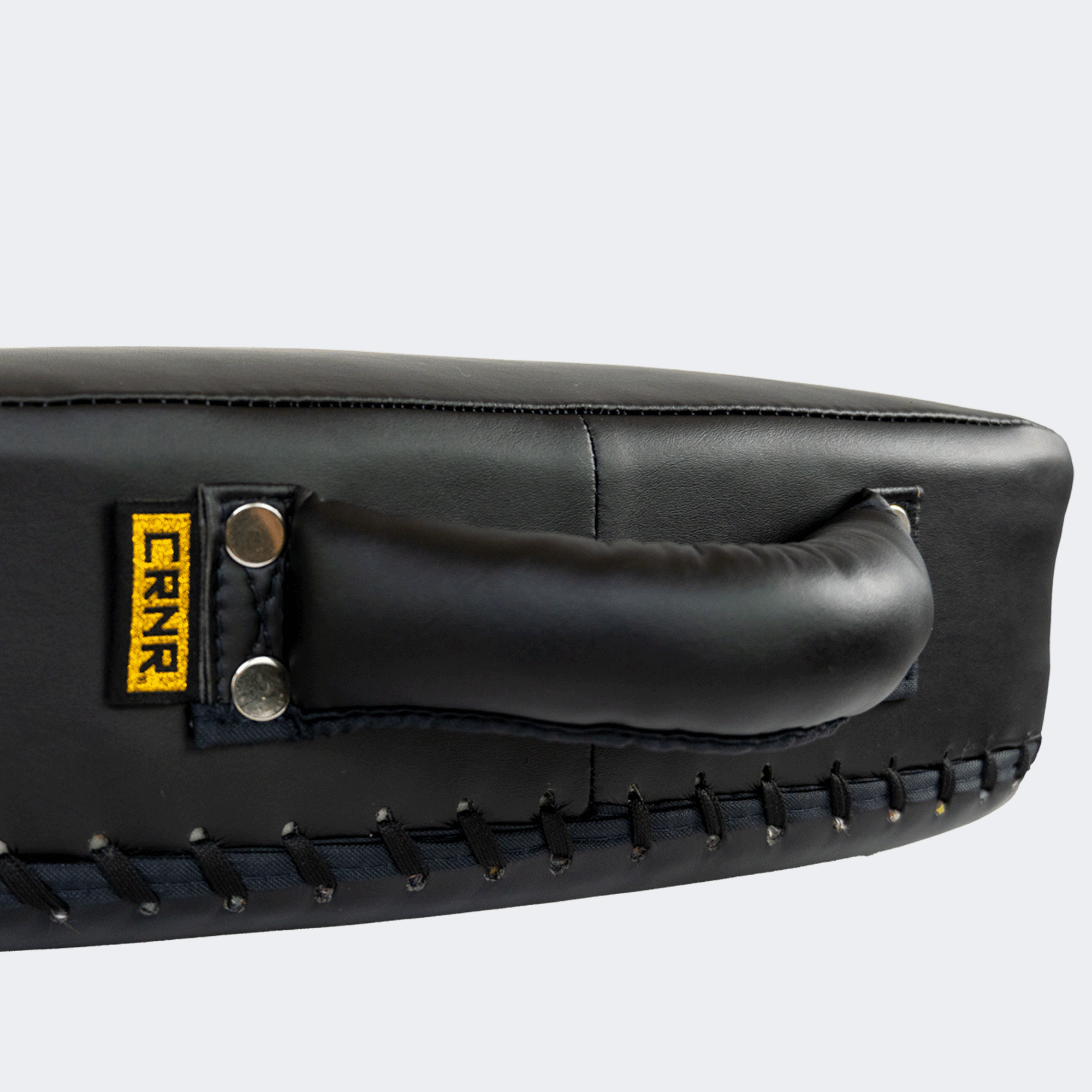 Top side view of the HMITV Low Kick Pad Lite, a large, black leather martial arts low kick shield pad by Combat Corner against a light grey background, featuring a white block "CRNR" logo on the striking surface.
