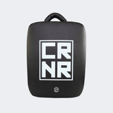 Front view of the HMITV Low Kick Pad Lite, a large, black leather martial arts low kick shield pad by Combat Corner against a light grey background, featuring a white block "CRNR" logo on the striking surface.