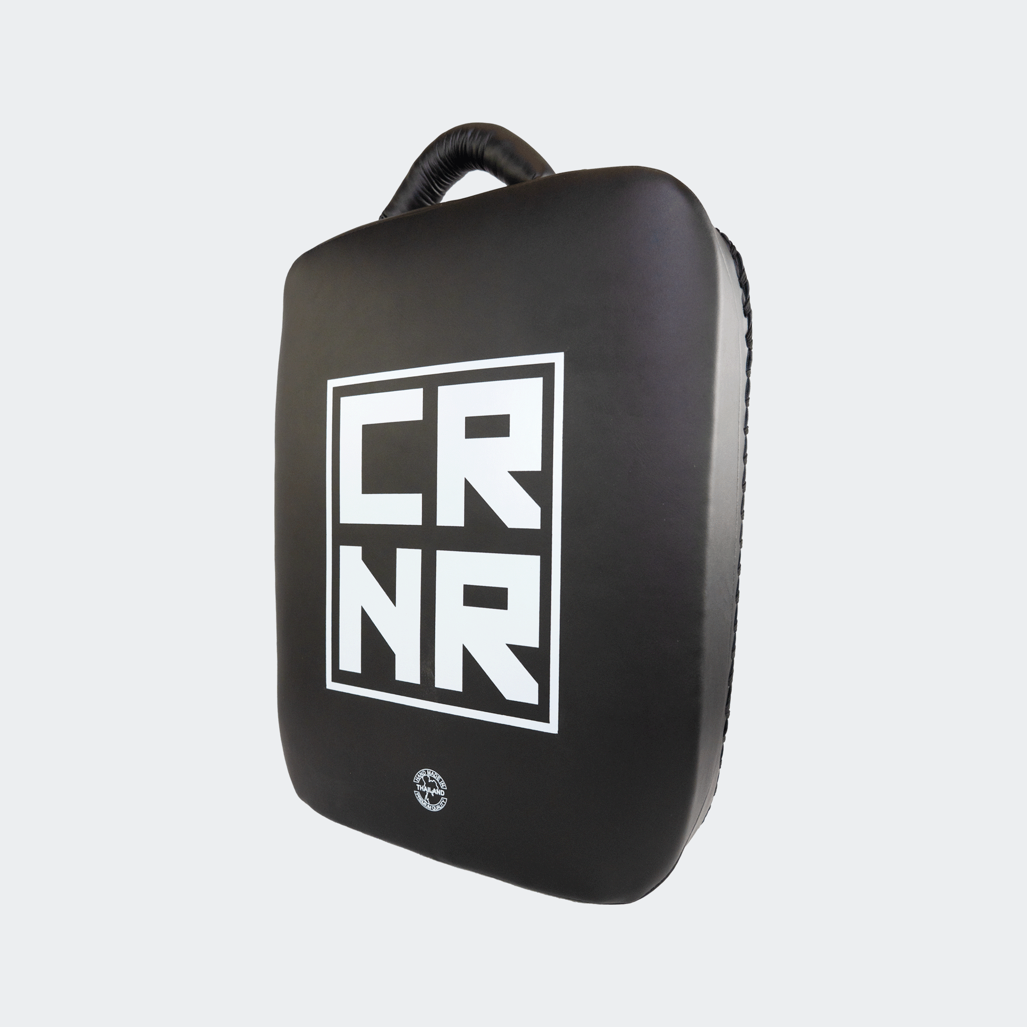 Front left angle view of the HMITV Low Kick Pad Lite, a large, black leather martial arts low kick shield pad by Combat Corner against a light grey background, featuring a white block "CRNR" logo on the striking surface.