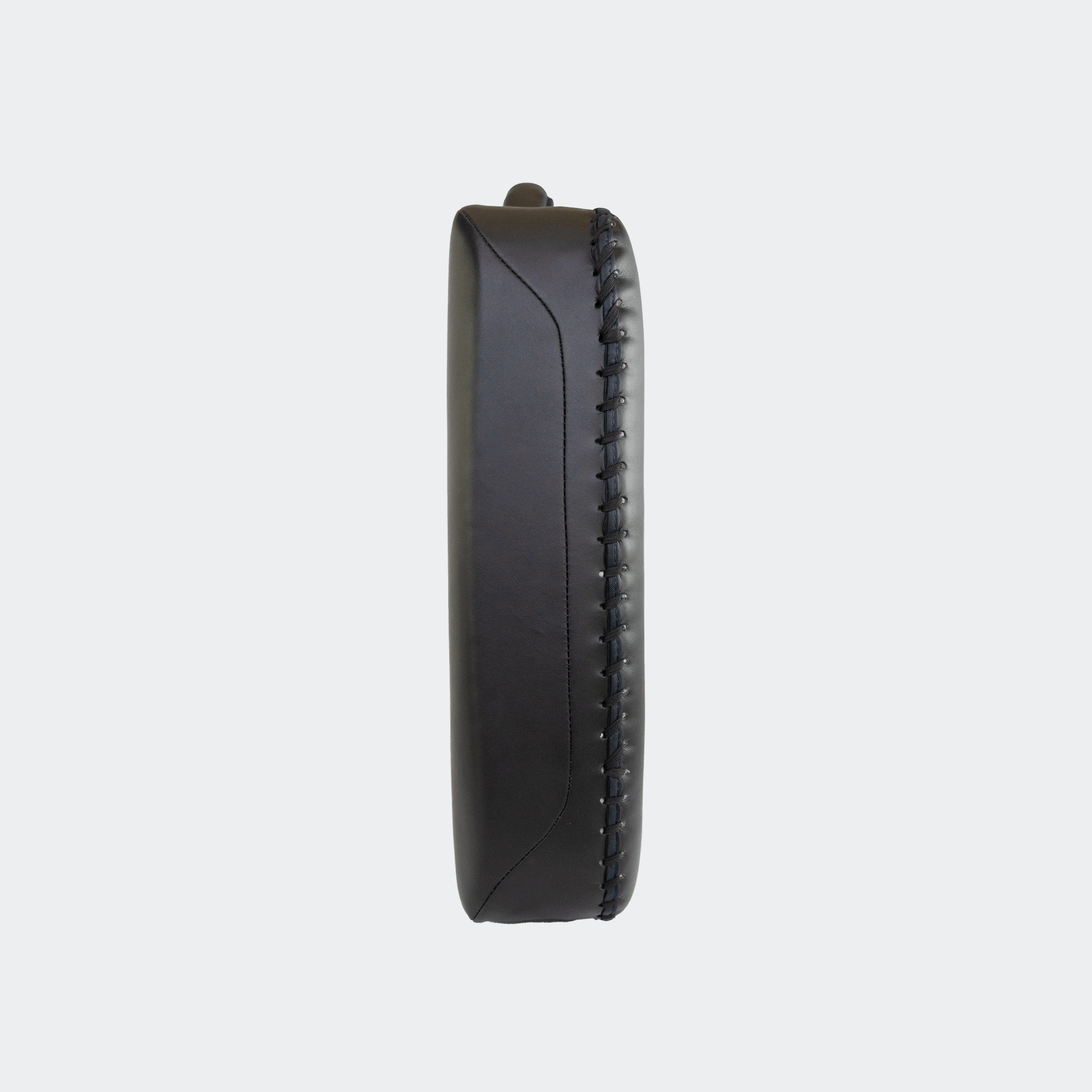 Side view of the HMITV Low Kick Pad Lite, a large, black leather martial arts low kick shield pad by Combat Corner against a light grey background, featuring a white block "CRNR" logo on the striking surface.