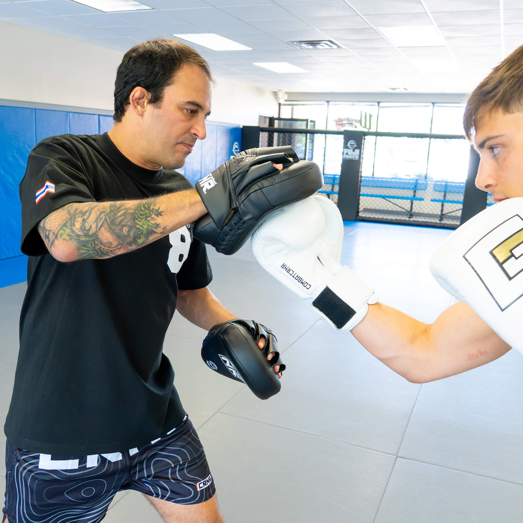 An action photograph of a boxing coach catching a punch with the black HMITV Curved Punch Mitts , as a fighter throws an uppercut wearing white Combat Corner boxing gloves.