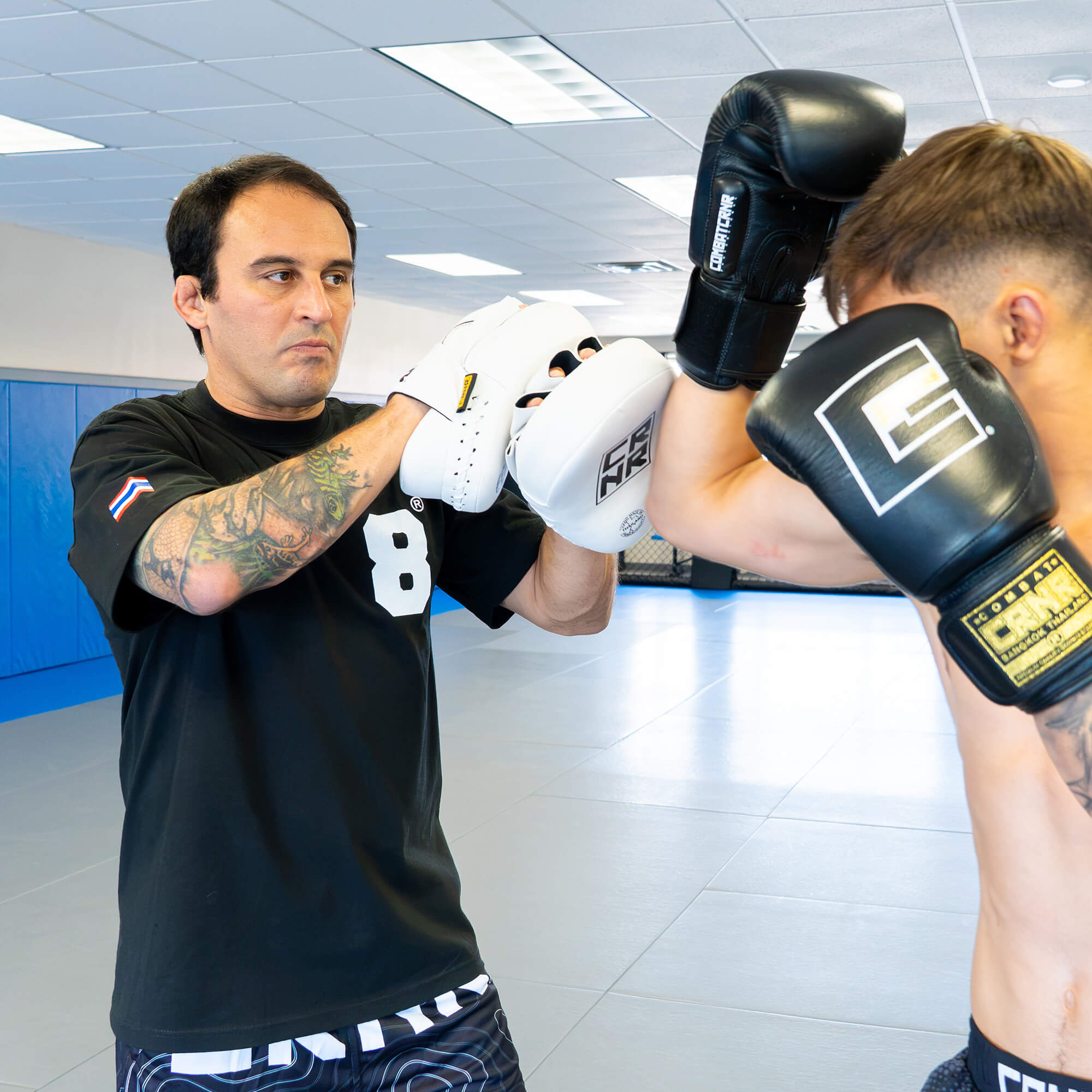 An action shot of a boxing trainer catching a close-range punch with the white HMITV Curved Punch Mitts, as a fighter strikes wearing black Combat Corner boxing gloves.