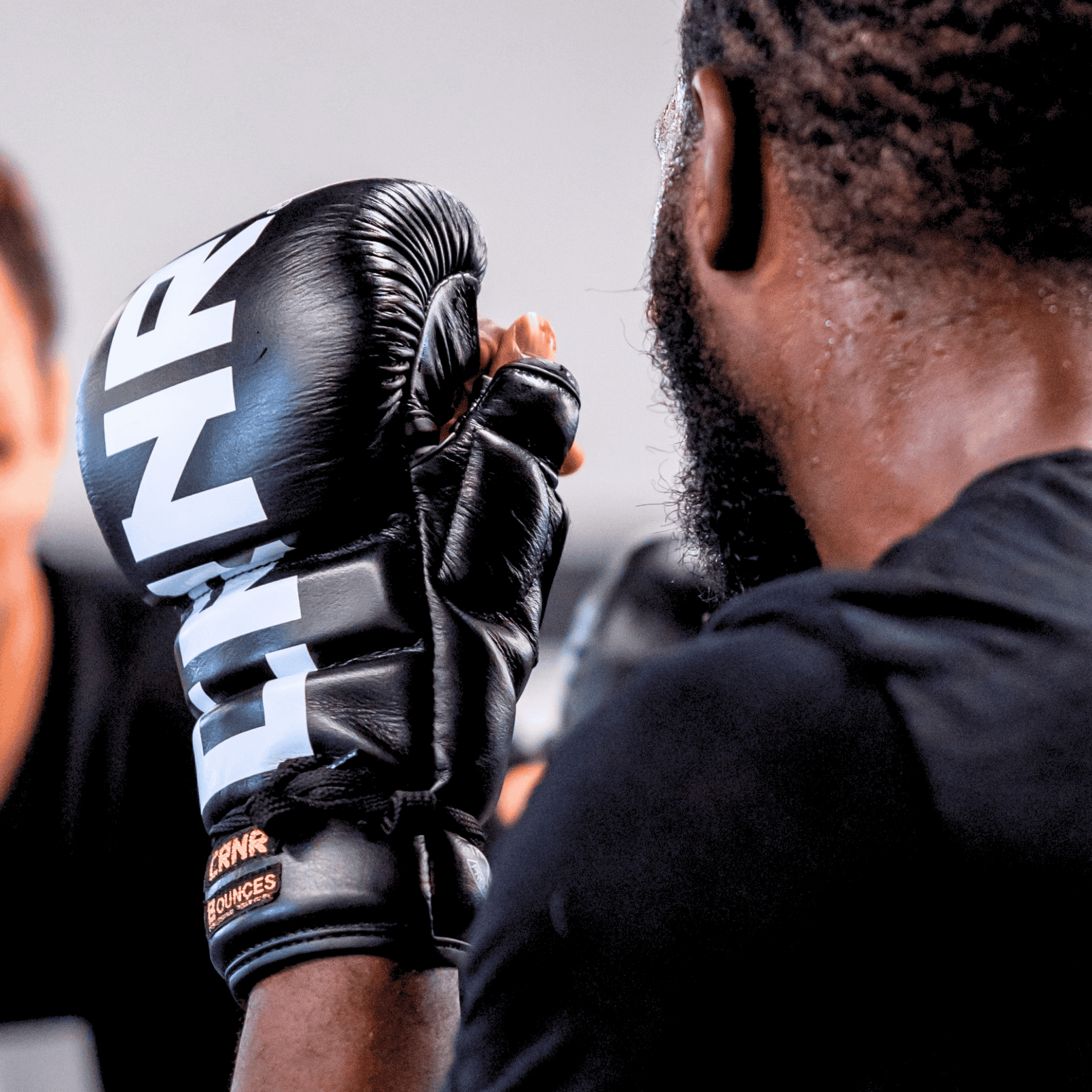 A photo of a pro fighter training with black Combat Corner HMIT Lace Up MMA Sparring Gloves during a sparring session. The photo shows a close up view of the HMIT Lace Up Sparring Gloves. 