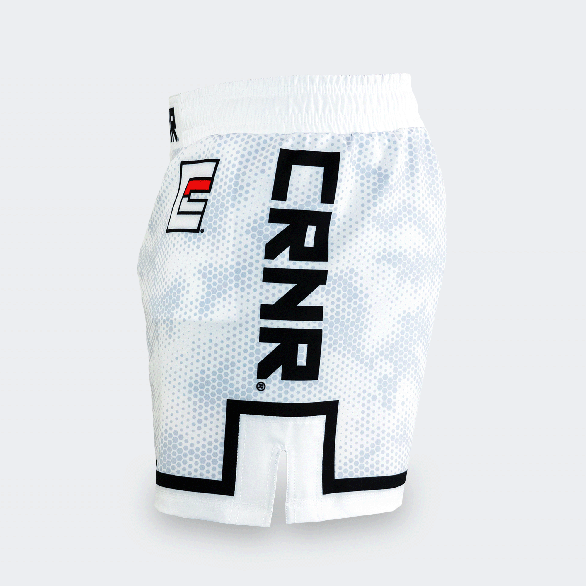 The left side view of the white CRNR ISO athletic fight shorts against a light gray background. The fabric showcases the white and gray hexagonal camo pattern. A large, bold black "CRNR" logo runs vertically down the side of the leg, framed at the bottom by a thick, angular black line that outlines the side hem slit. Towards the front hip area, a smaller square logo features a stylized black letter "E" with a red horizontal stripe inside.