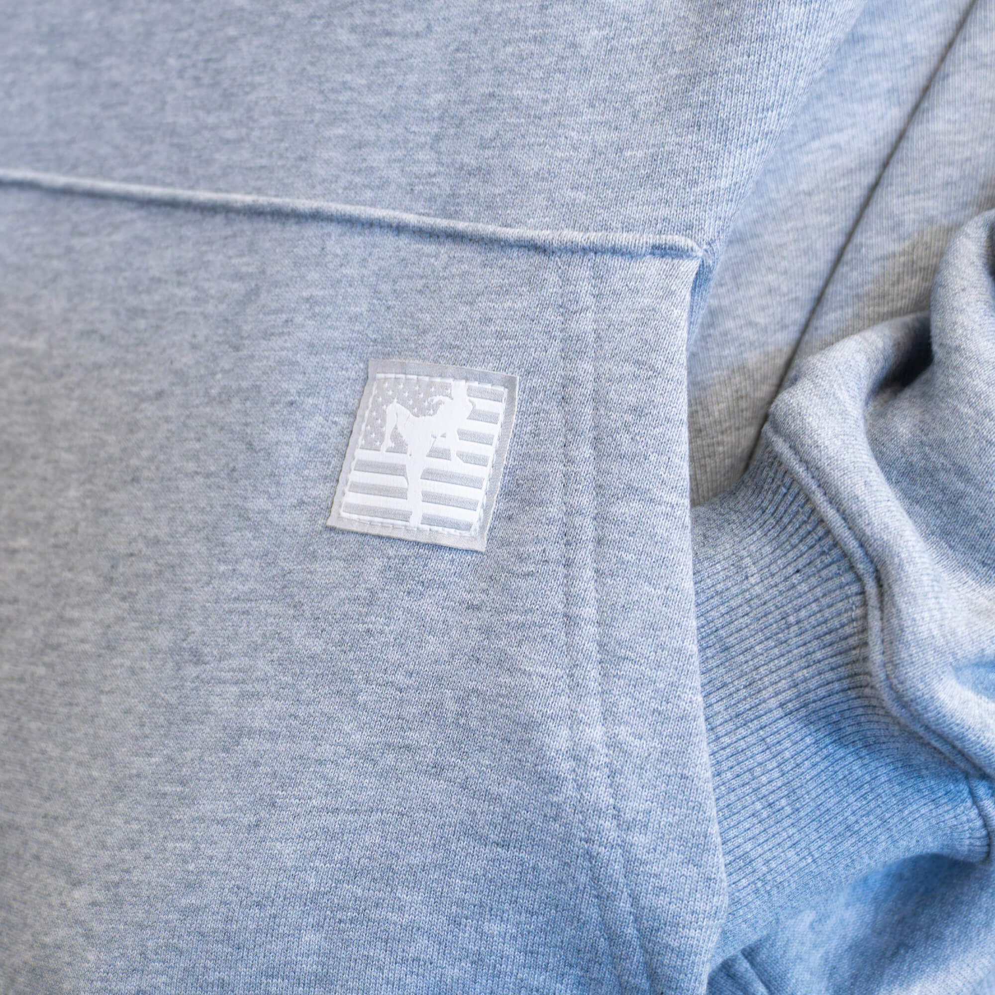 Close-up detail of the kangaroo pocket on a gray Combat Corner hoodie, showcasing the stitched woven patch featuring a silhouette of a Muay Thai fighter over an American flag design.