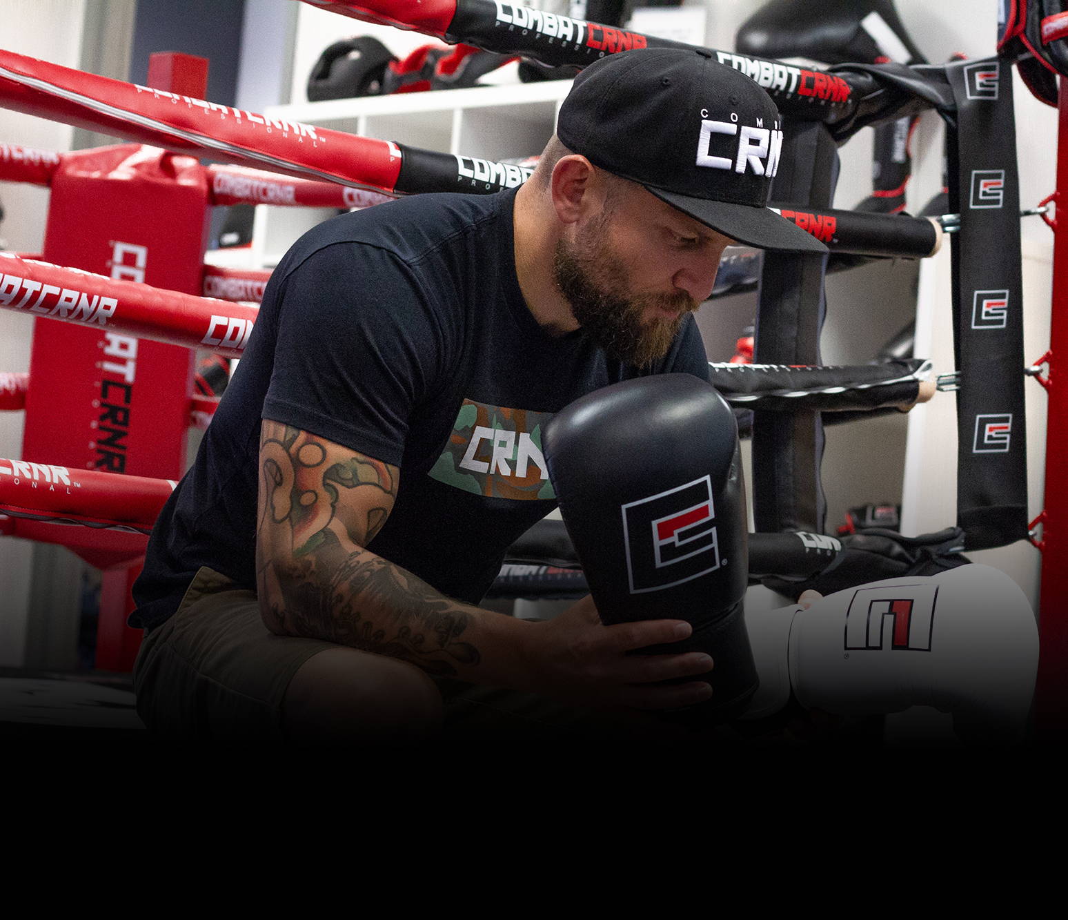 Portrait of Combat Corner founder Dan LaSavage sitting on the edge of a Combat Corner boxing ring inspecting a pair of Combat Corner Boxing Gloves.