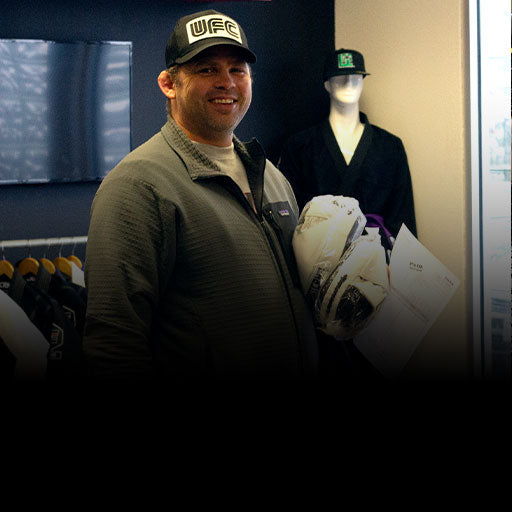 A gym owner holding papers and Combat Corner punch mitts in a room with mannequins and sports equipment.
